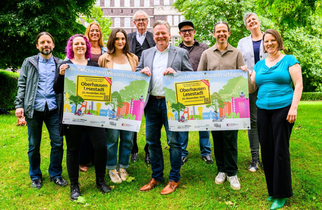 Oberbürgermeister Thorsten Berg präsentiert zusammen mit Mitarbeitenden das Plakat zur Lesestadt 2026