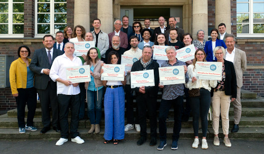 Oberbürgermeister Daniel Schranz (2. v.l.), Beigeordneter Michael Jehn (3. v.l.), CIO Boris van Benthem (Mitte oben), Jurymitglieder, die Antragsstellerinnen und Antragssteller der geförderten Projekte sowie das Smart City Team. Foto: Stadt Oberhausen