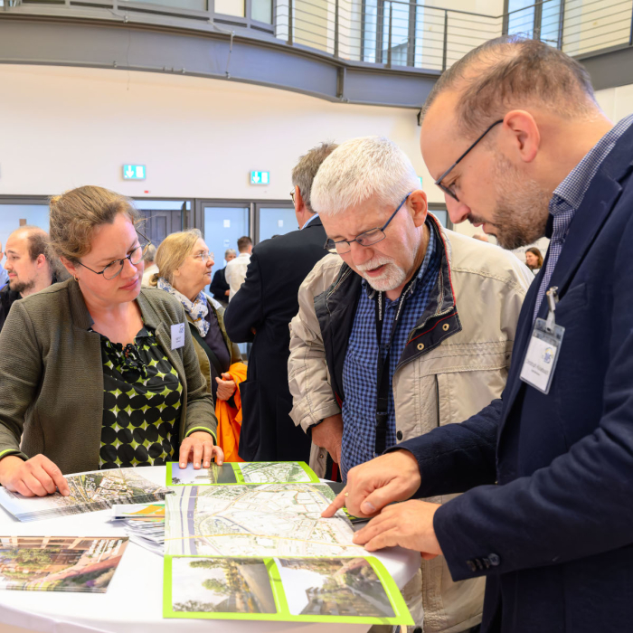 Ein Mann (Bildmitte) wird von einem anderen mann etwas in einer Broschüre erklärt, eine Frau schaut dabei zu. (Foto: Stadt Oberhausen/Tom Thöne