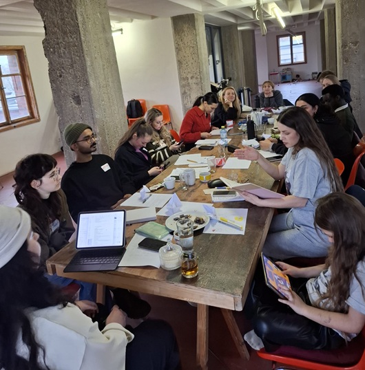 Menschen sitzen um einen Tisch herum und arbeiten konzentriert an Texten