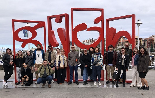 Eine größere Gruppe von Menschen vor einer Skulptur des Schriftzugs Gijon