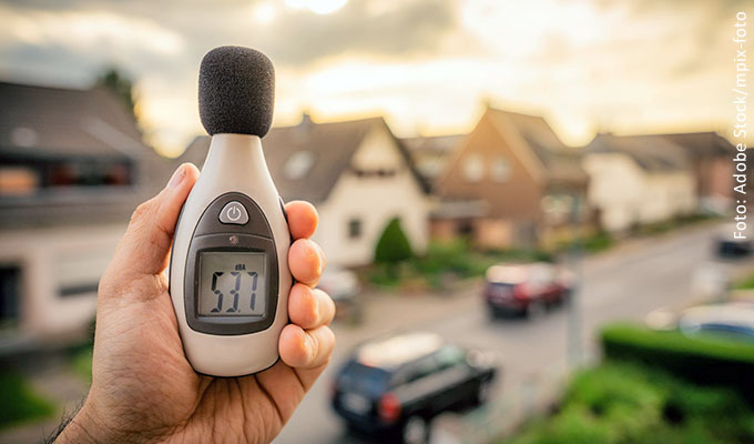 Geräuschmessgeräte in einer Hand gehalte und im Hintergrund eine Wohnsiedlung