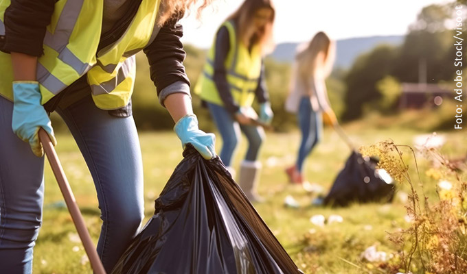 Menschen sammeln mit Greifzangen Müll auf einer Wiese ein