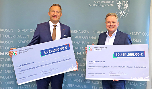 Regierungspräsident Thomas Schürmann (li.) übergab Oberbürgermeister Thorsten Berg die beiden symbolischen Schecks. (Foto: Stadt Oberhausen)